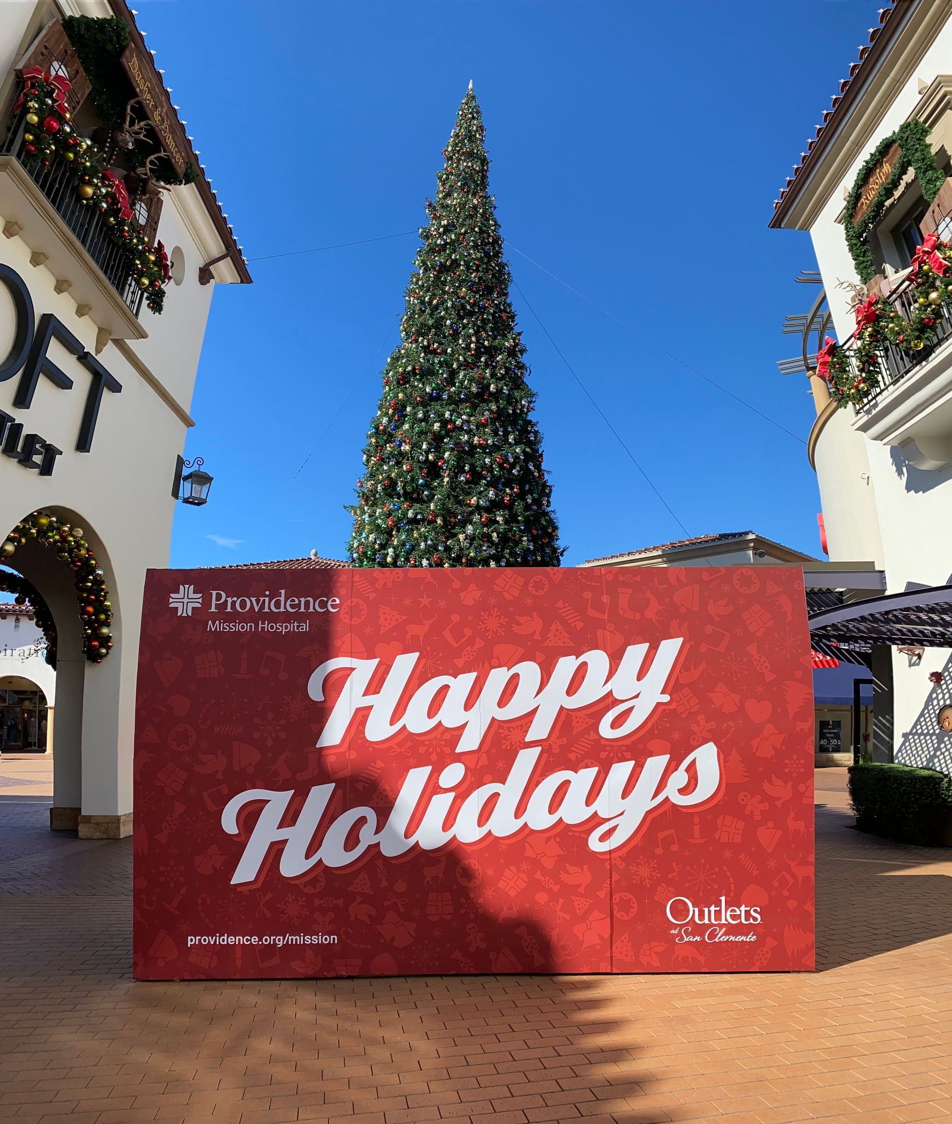 A large red sign that says `` happy holidays '' is in front of a christmas tree.