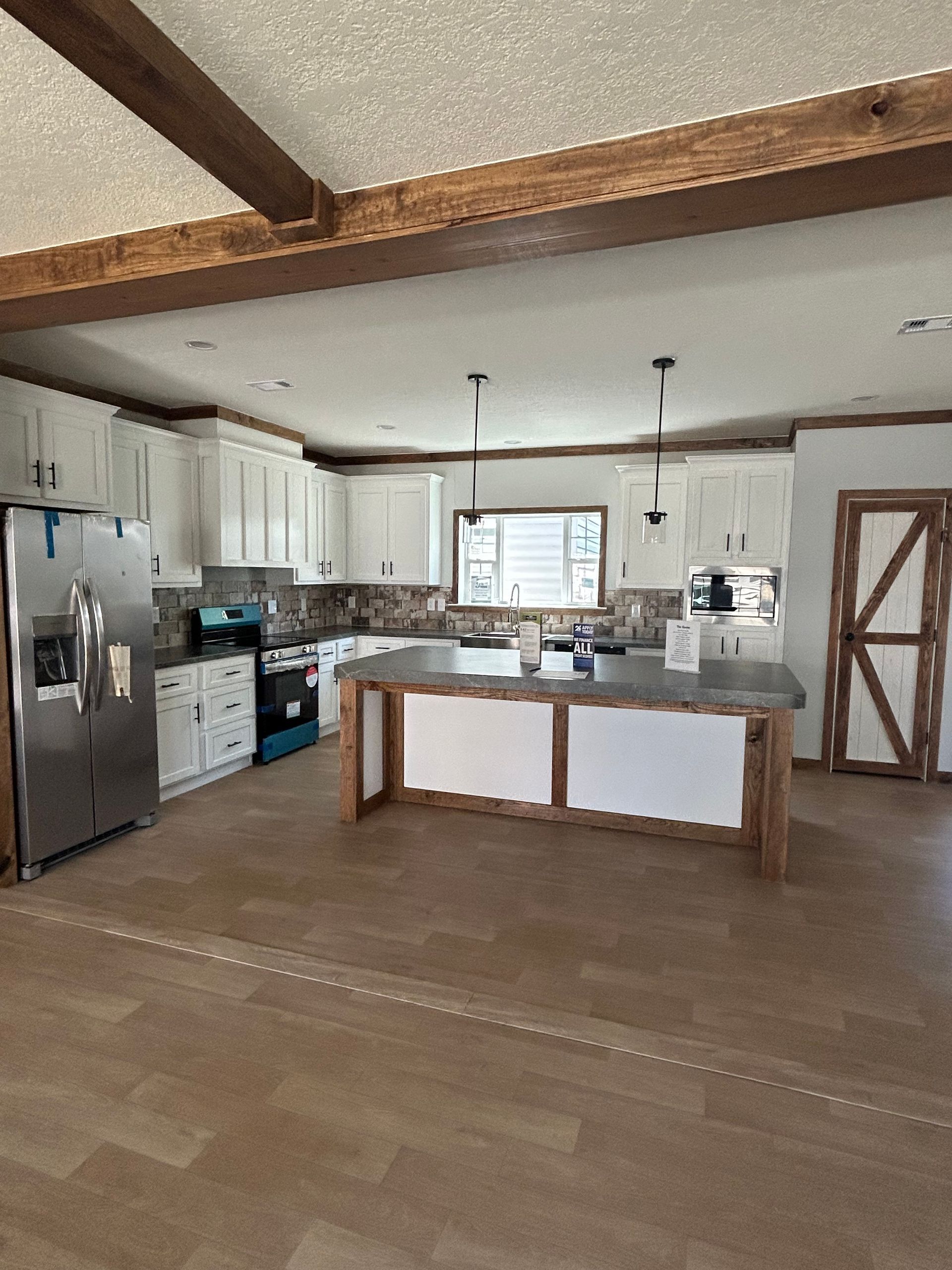 A spacious kitchen with white cabinets, stainless steel appliances, and a large island with a gray countertop.