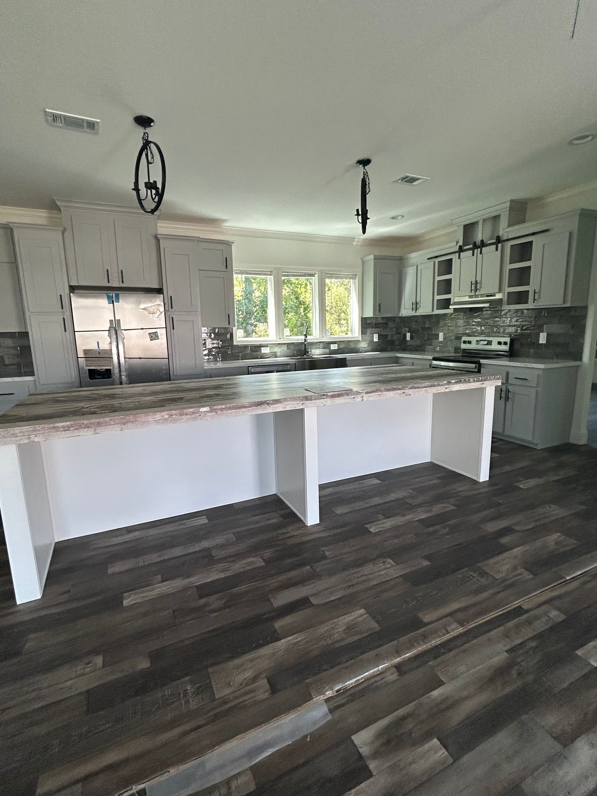 Interior view of a modern kitchen with a large island, white cabinets, and gray-brown wood-look flooring.