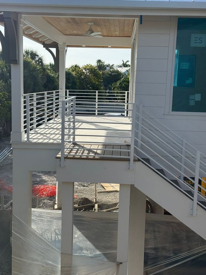 Covered outdoor walkway with white railings and stairs beside a building, overlooking trees and water below