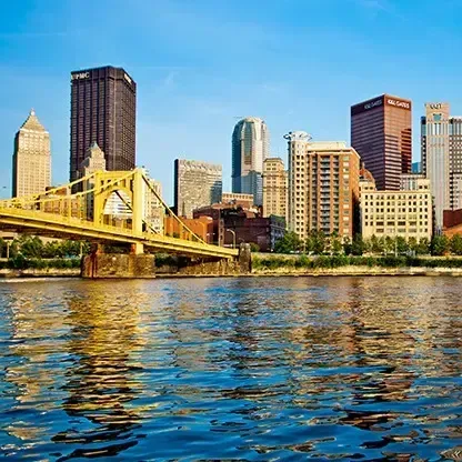 Pittsburgh skyline with a golden bridge over a blue river under a clear sky.