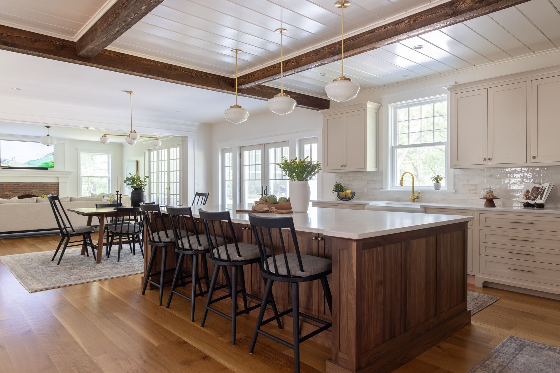 A bright kitchen with a wooden island and black bar stools, featuring white cabinetry, pendant lights, and wood floors.