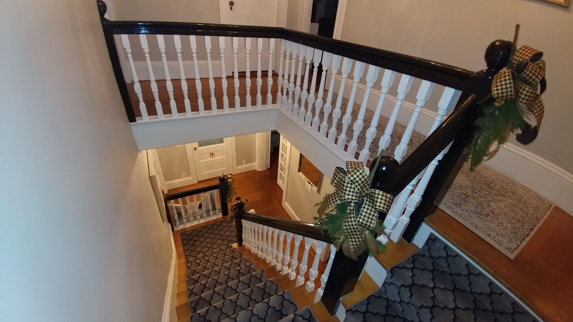 An L-shaped staircase with black handrails, white spindles, and patterned blue carpet, decorated with holiday ribbons.