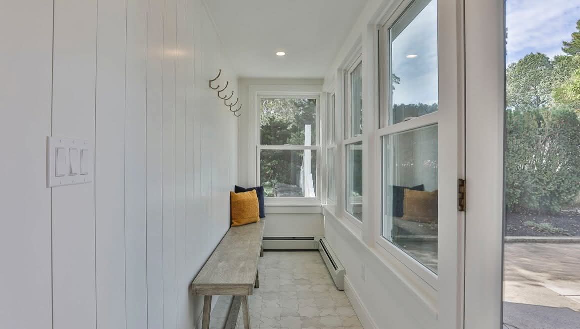 White entryway with bench, coat hooks, windows overlooking greenery.