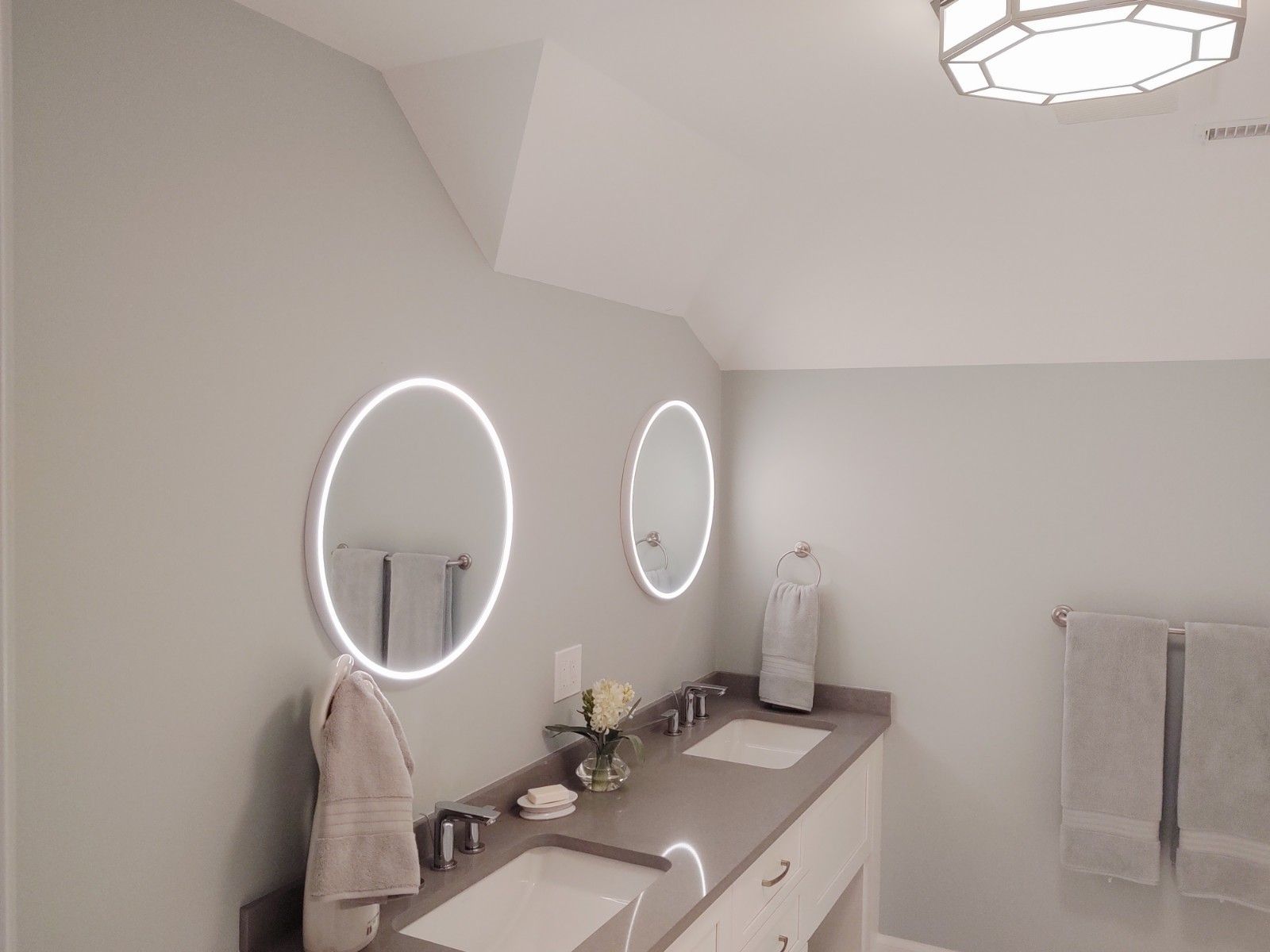Bathroom with oval mirrors, gray walls, double sink, and a modern light fixture.