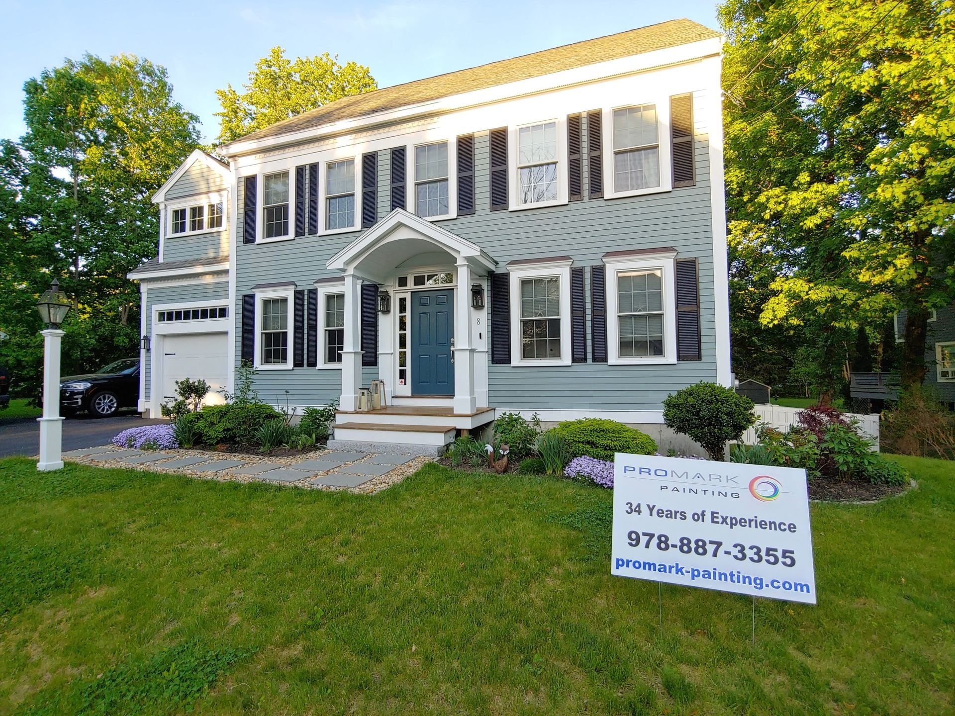 Two-story house with blue siding, black shutters, and a dark blue front door; a sign in the yard.