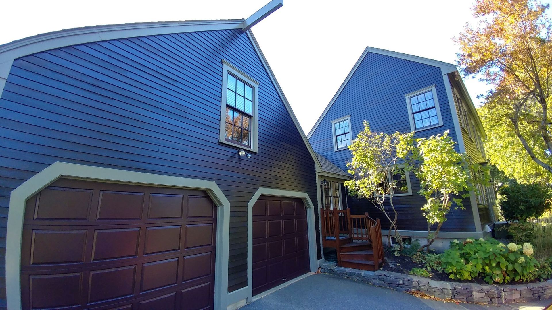 Blue house with brown garage doors and a porch, surrounded by trees.