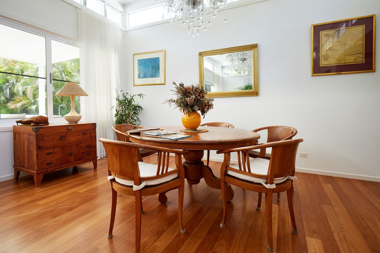 Dining room with round wooden table, chairs, art, chest, and chandelier.