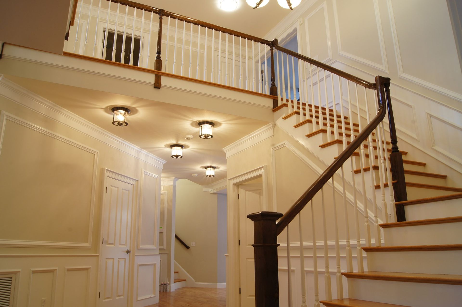A two-story entryway with a wooden staircase and a balcony, cream walls, and white molding.