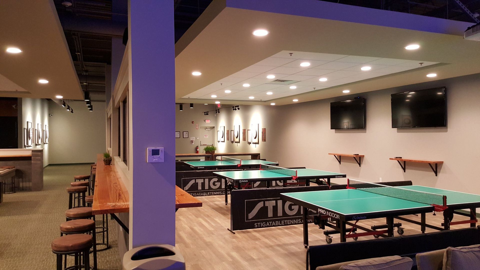 Ping pong room with multiple tables, TVs, and seating.