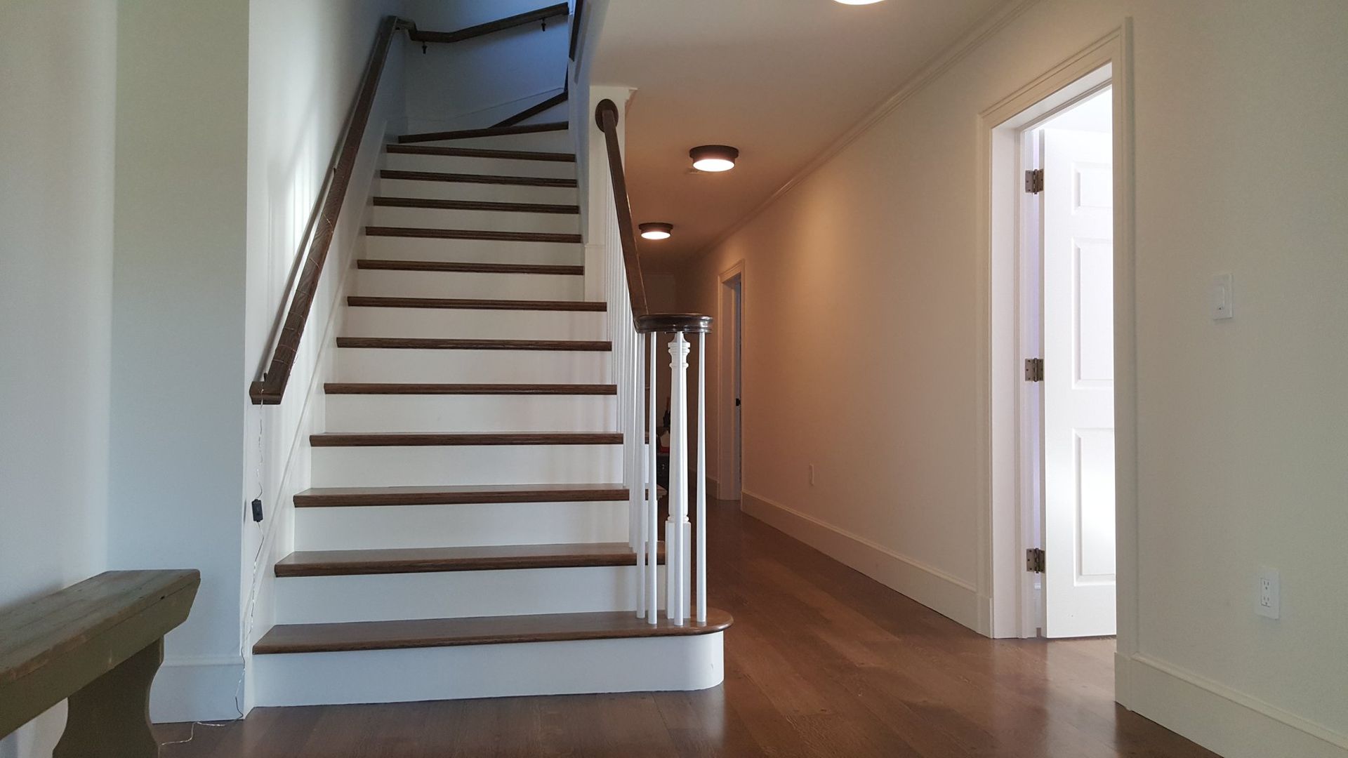 Interior hallway with staircase, white walls, wood floors, and recessed lighting.