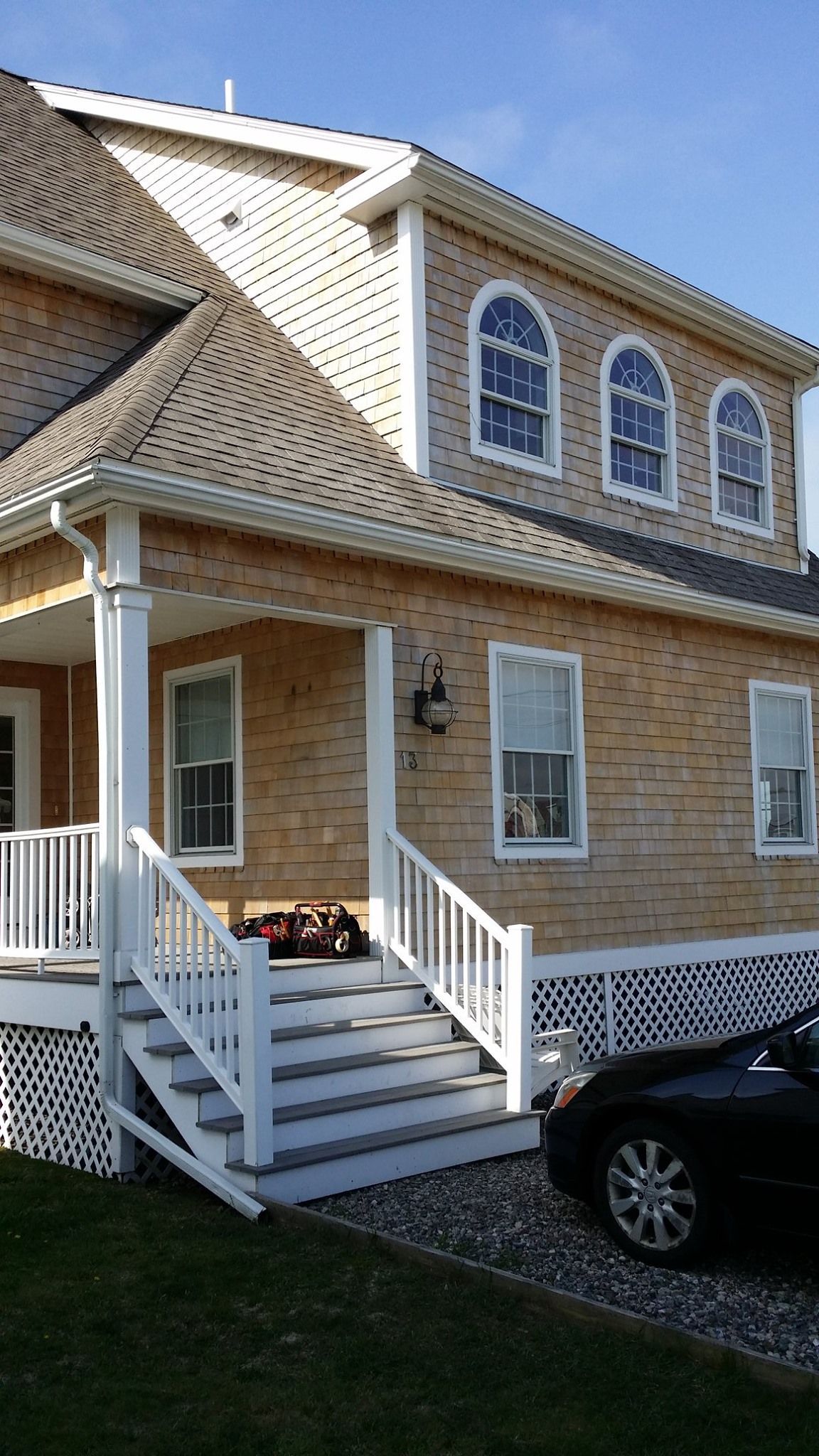 Two-story wooden house with white trim. Porch, steps, and a car parked in front.