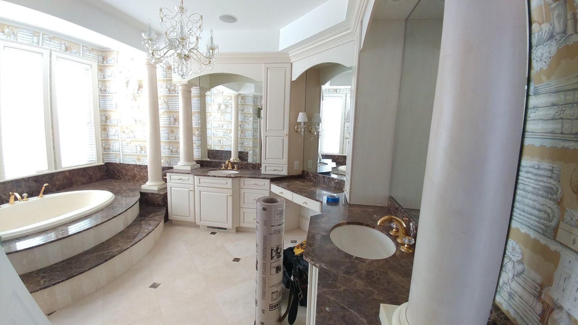 Luxurious bathroom with a tub, sinks, columns, and chandelier.