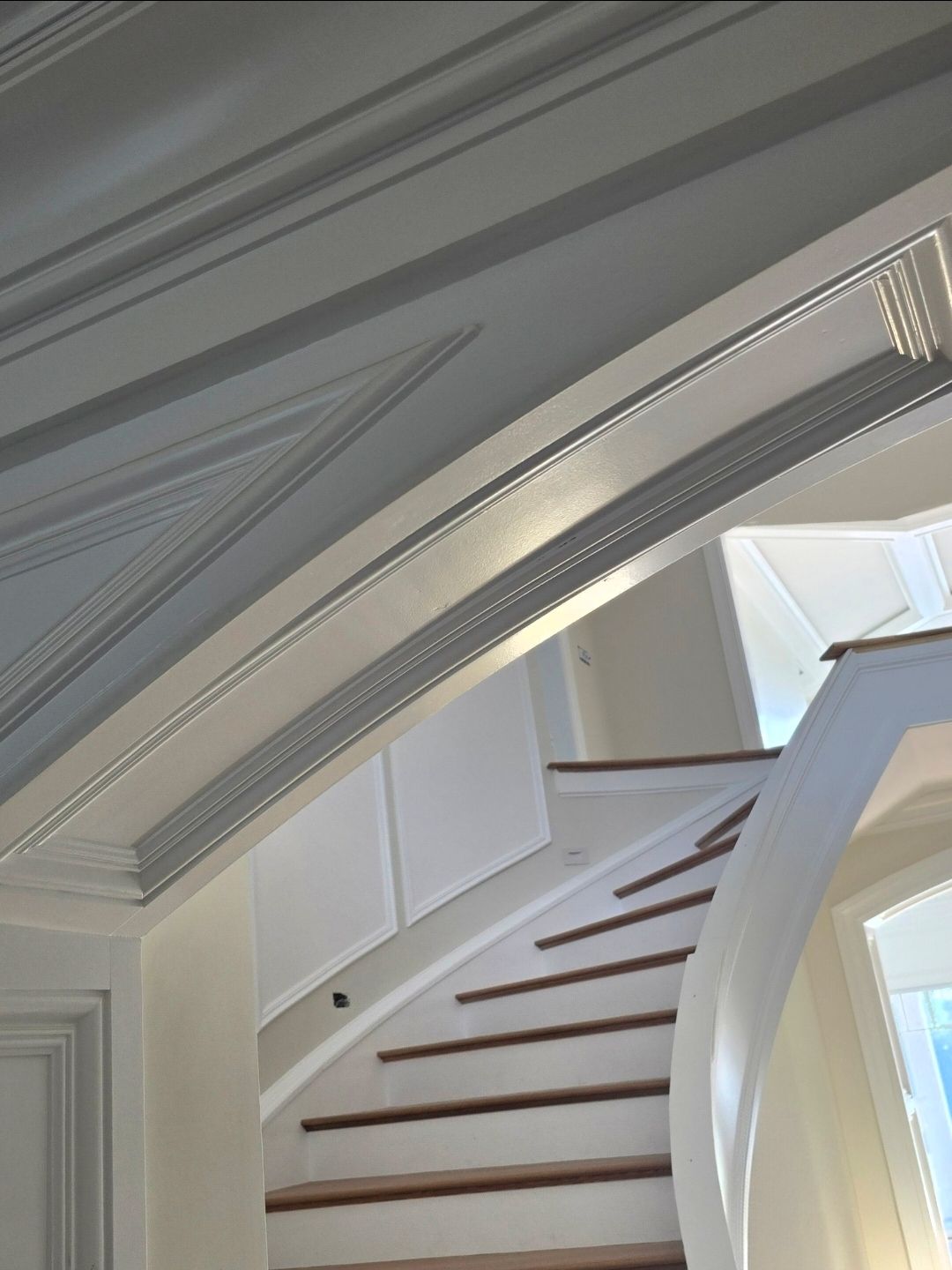 Staircase with wooden steps and white banister, leading upwards; light and shadows on the ceiling.