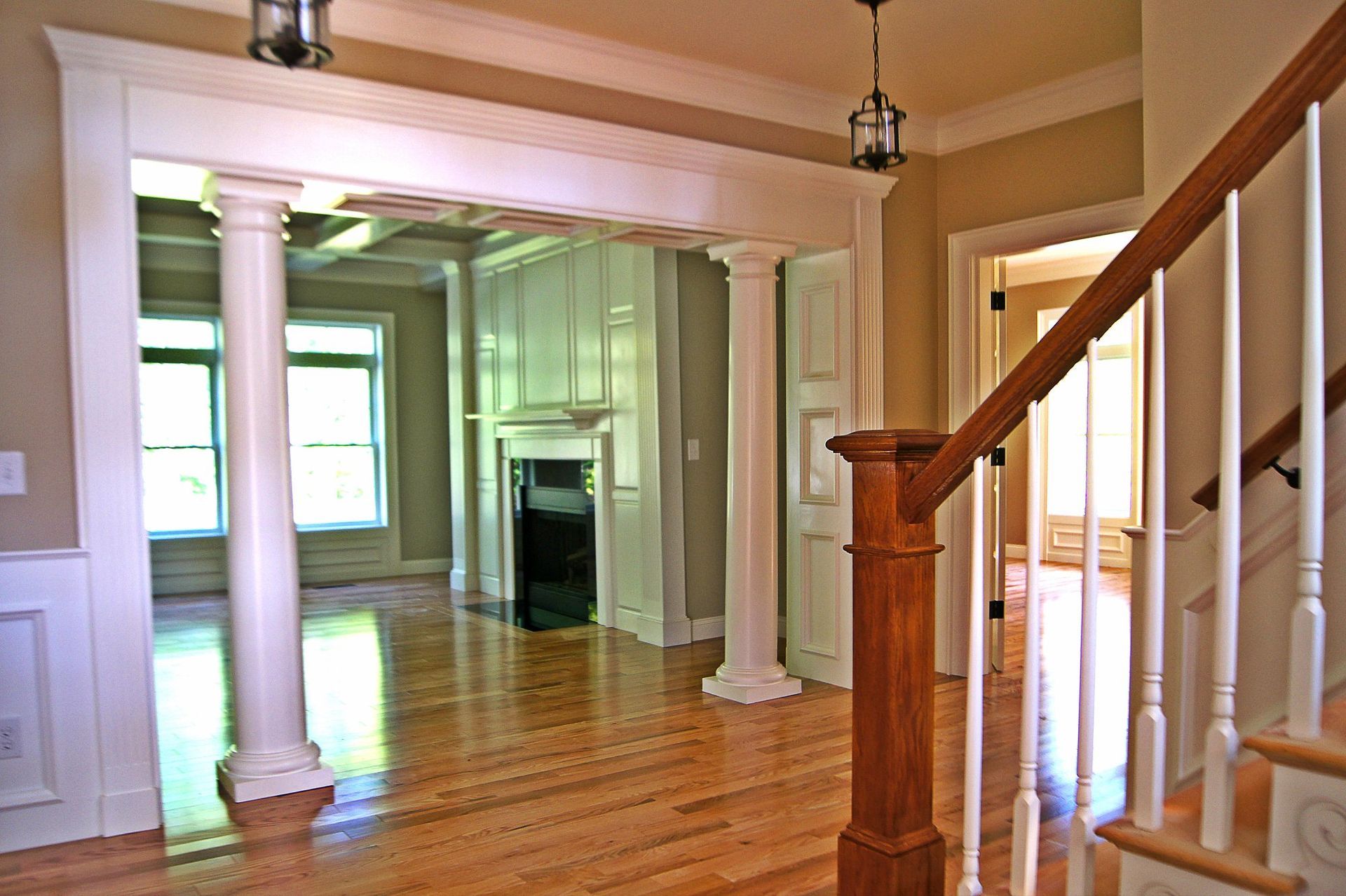 Wooden-floored entry hall with staircase and ornate white pillars leading to a living area with fireplace.