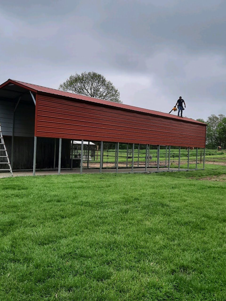 Person on red roof of a large barn-like structure, possibly trimming trees. Overcast day.