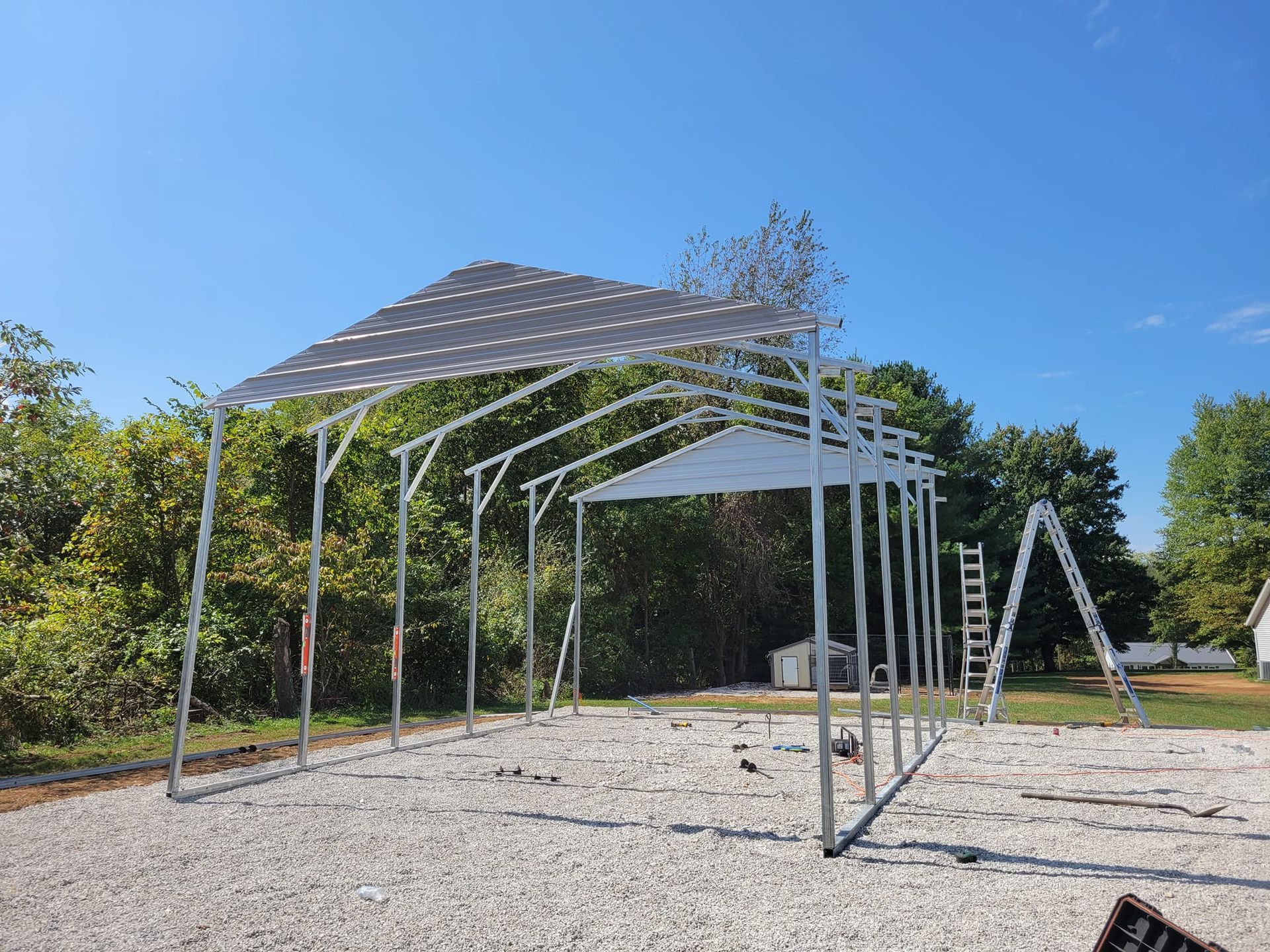 Partially constructed metal carport on a gravel surface under a clear blue sky.