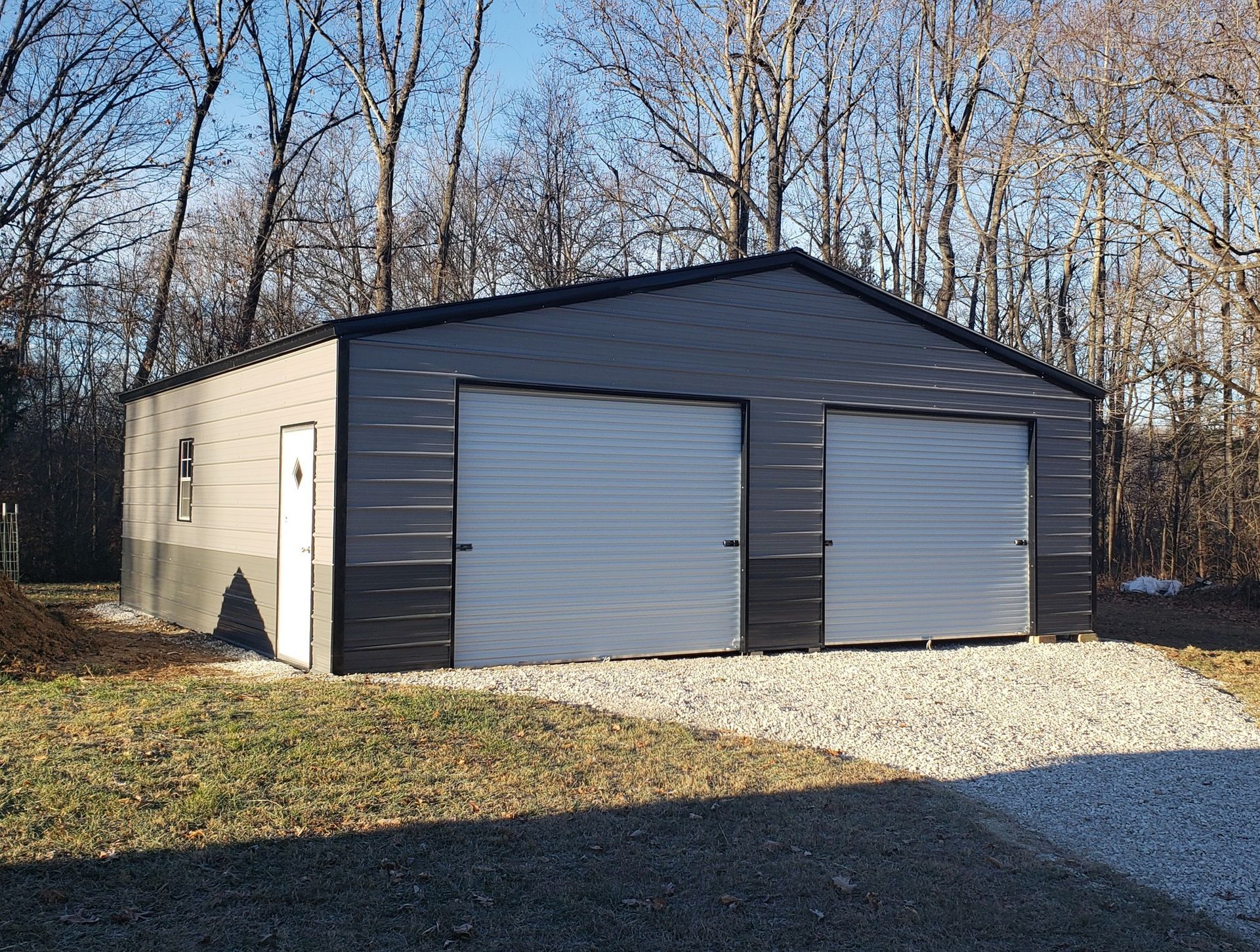 Two-car garage with gray siding and black trim, two garage doors, and a small side door; set in a yard.
