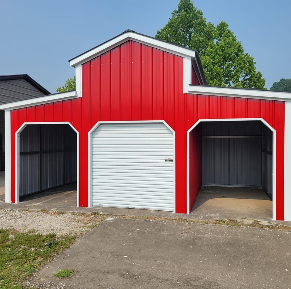 Red and white barn-style structure with a garage door and open storage bays, on a paved surface.