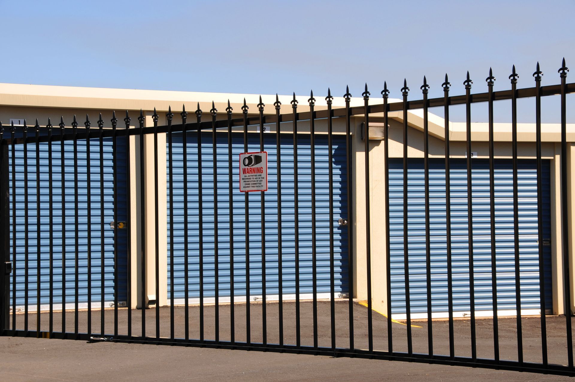Black metal gate in front of a white garage door with a small warning sign.