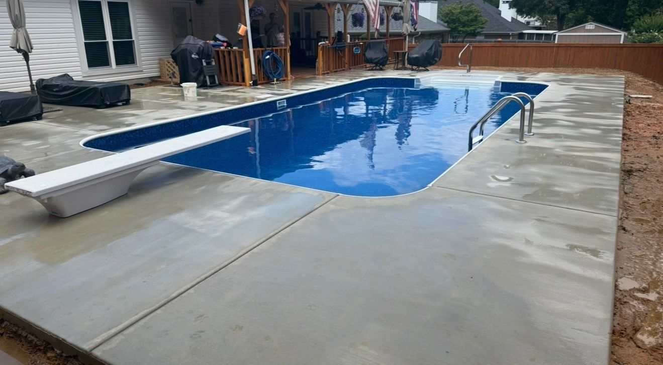 Blue pool with concrete deck, diving board, and handrail. Outdoors, daytime.