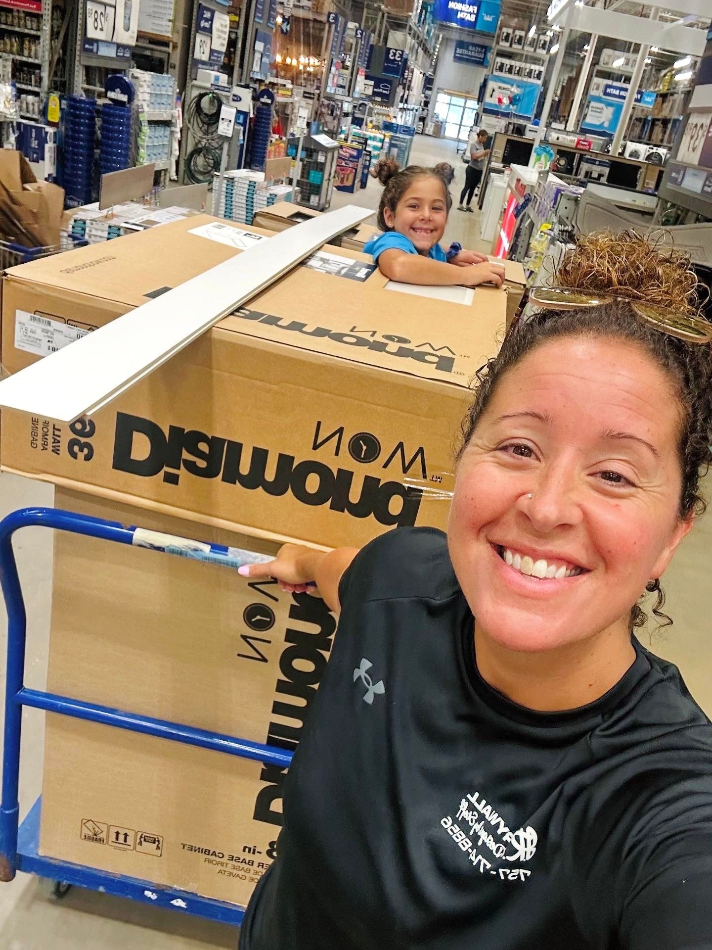 Woman and child in a Lowe's store, child in a large box on a cart, smiling at the camera.