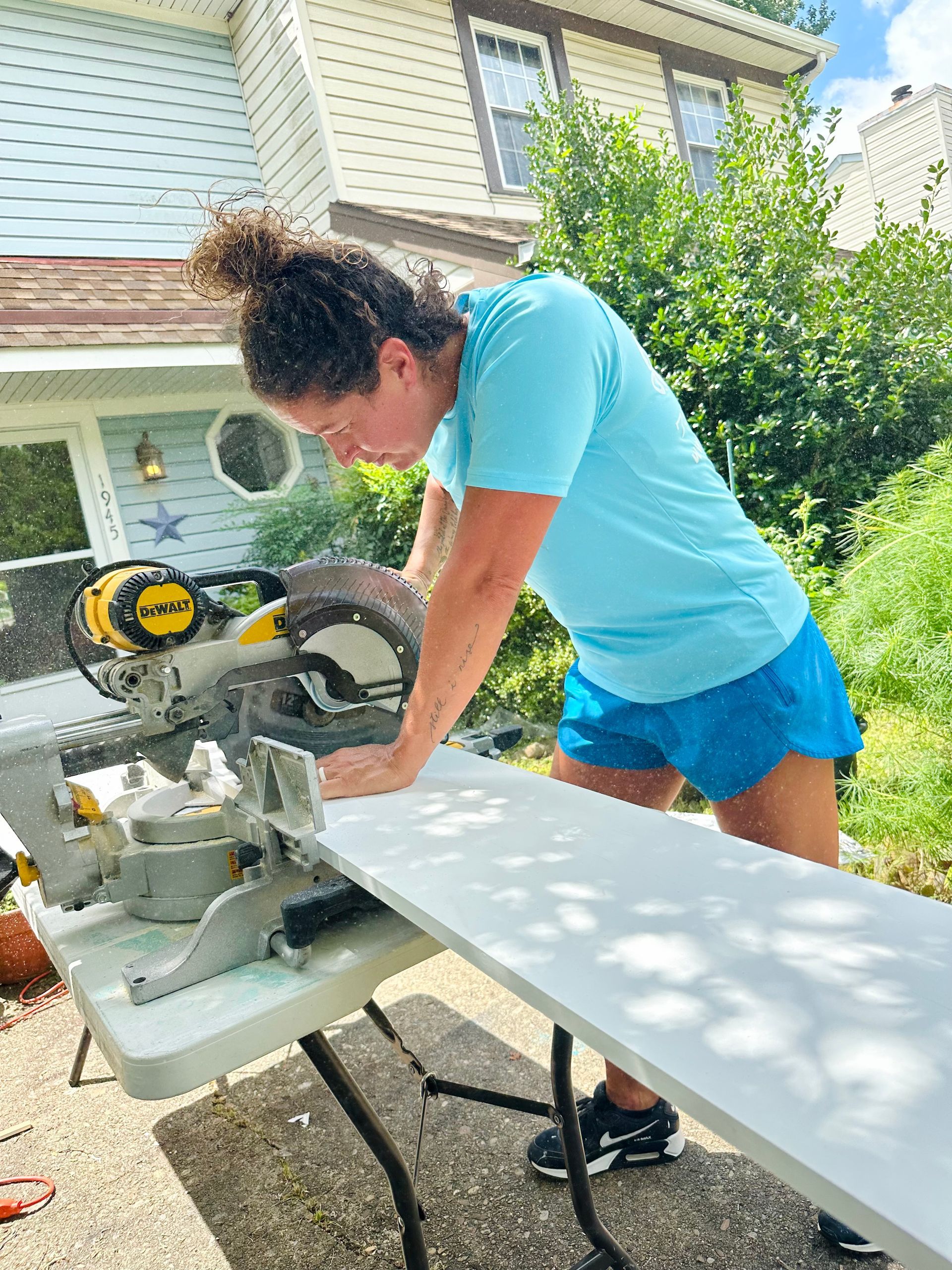 Woman in blue cuts wood with a saw outside a house.