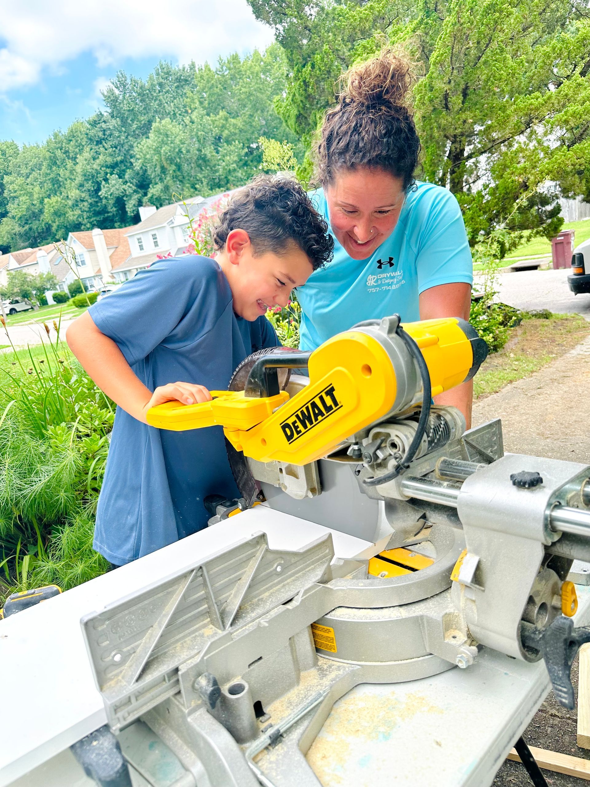 A woman and a boy using a yellow saw together outside.