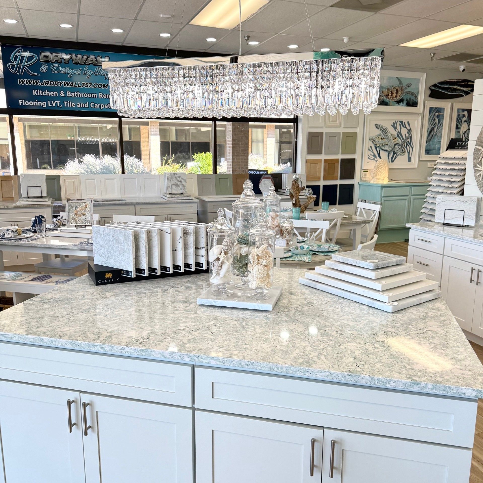 Kitchen showroom with white cabinets, granite countertop, and chandelier lighting.
