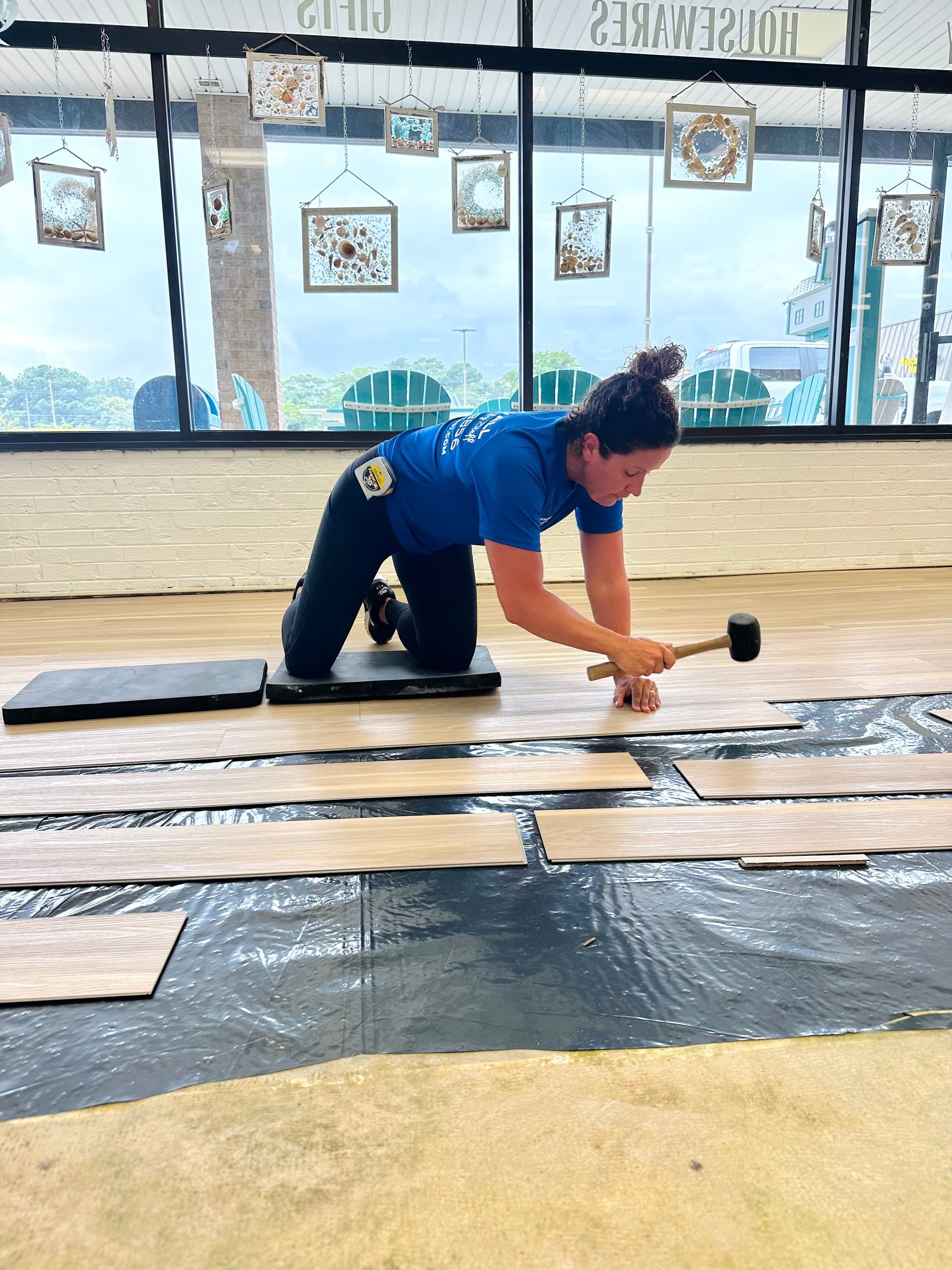 Woman kneeling, hammering floorboards indoors, installing flooring.