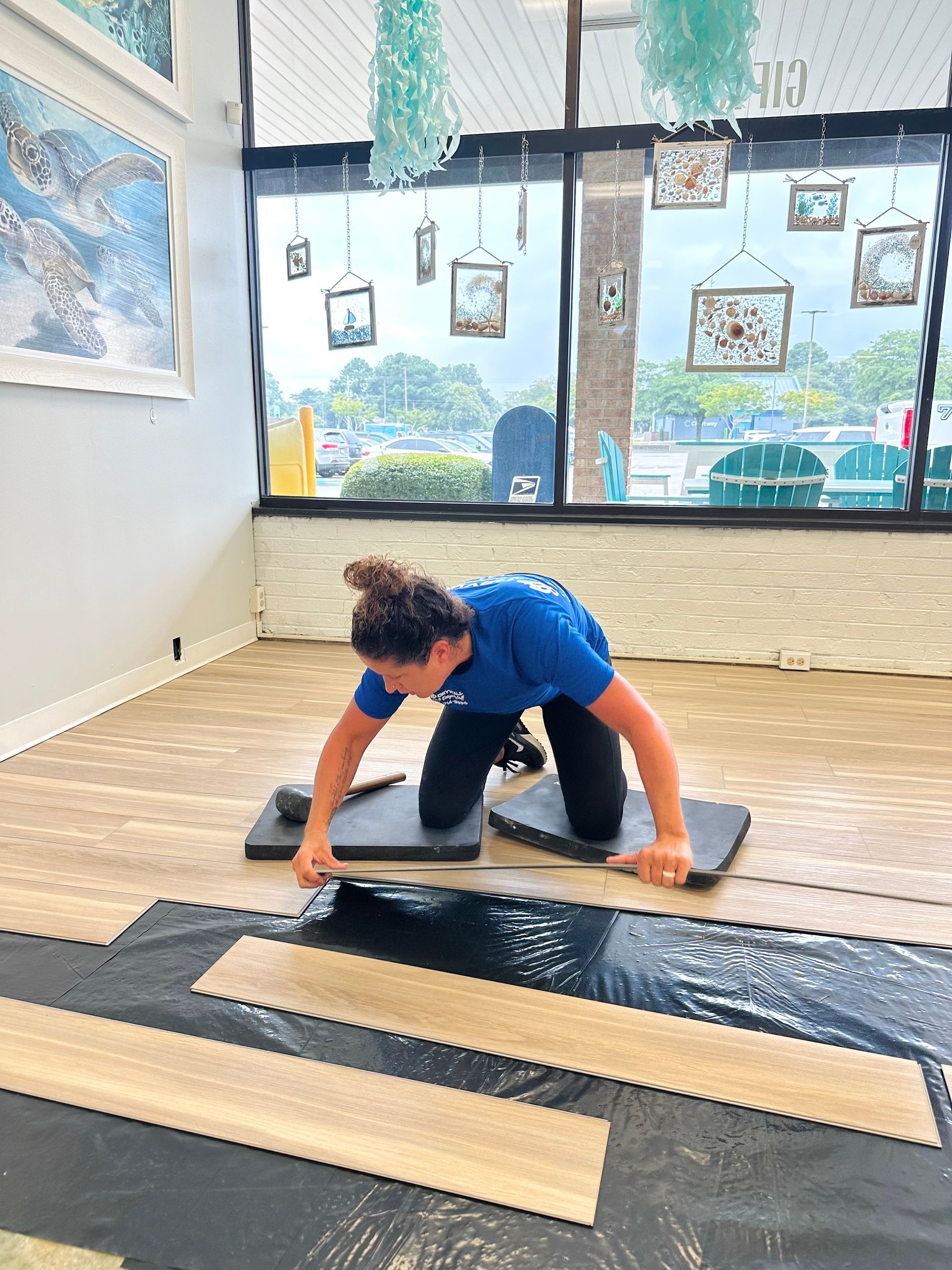Woman on her knees installing flooring, indoors near a window.