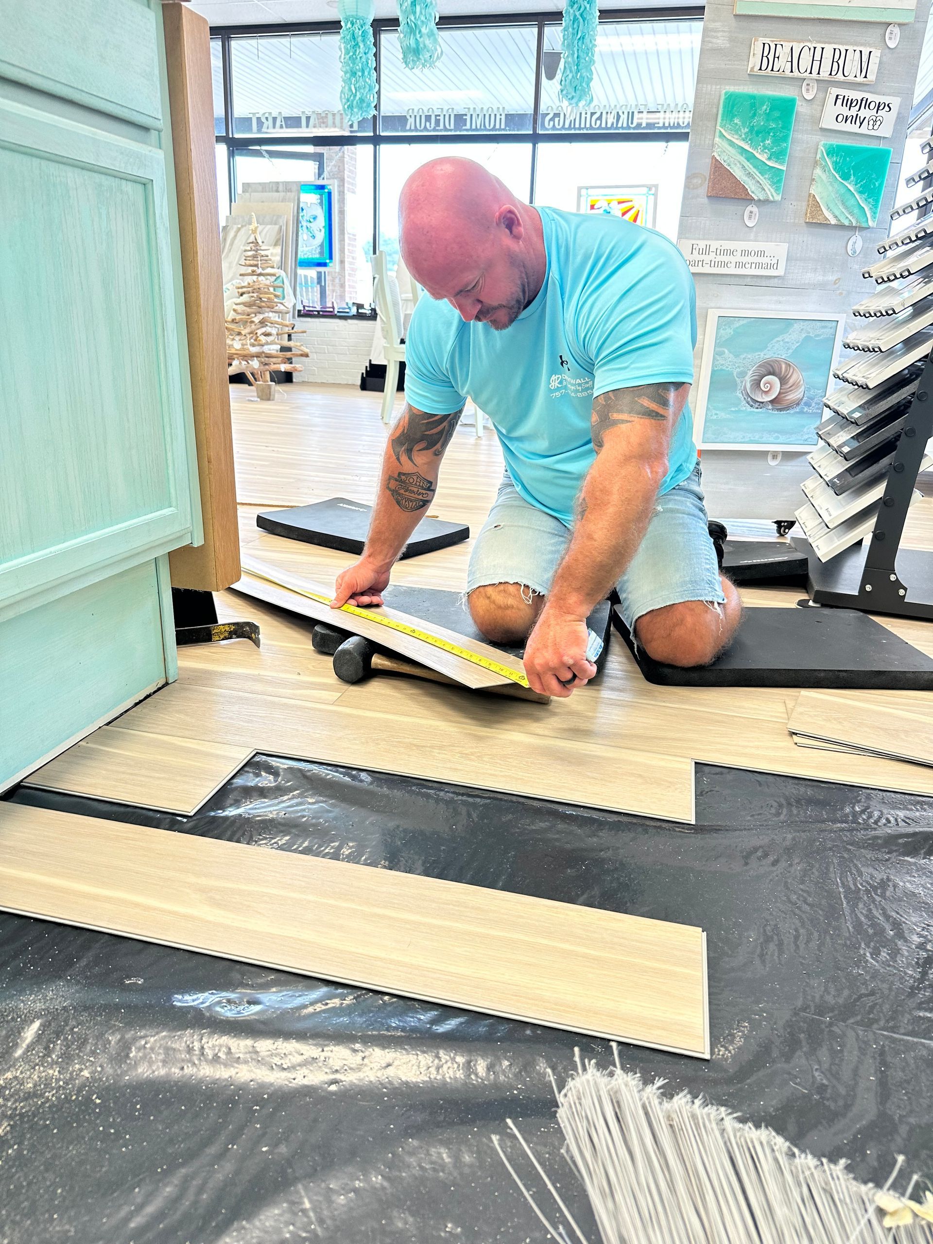 Man kneels, measuring flooring in a shop with blue-themed décor.