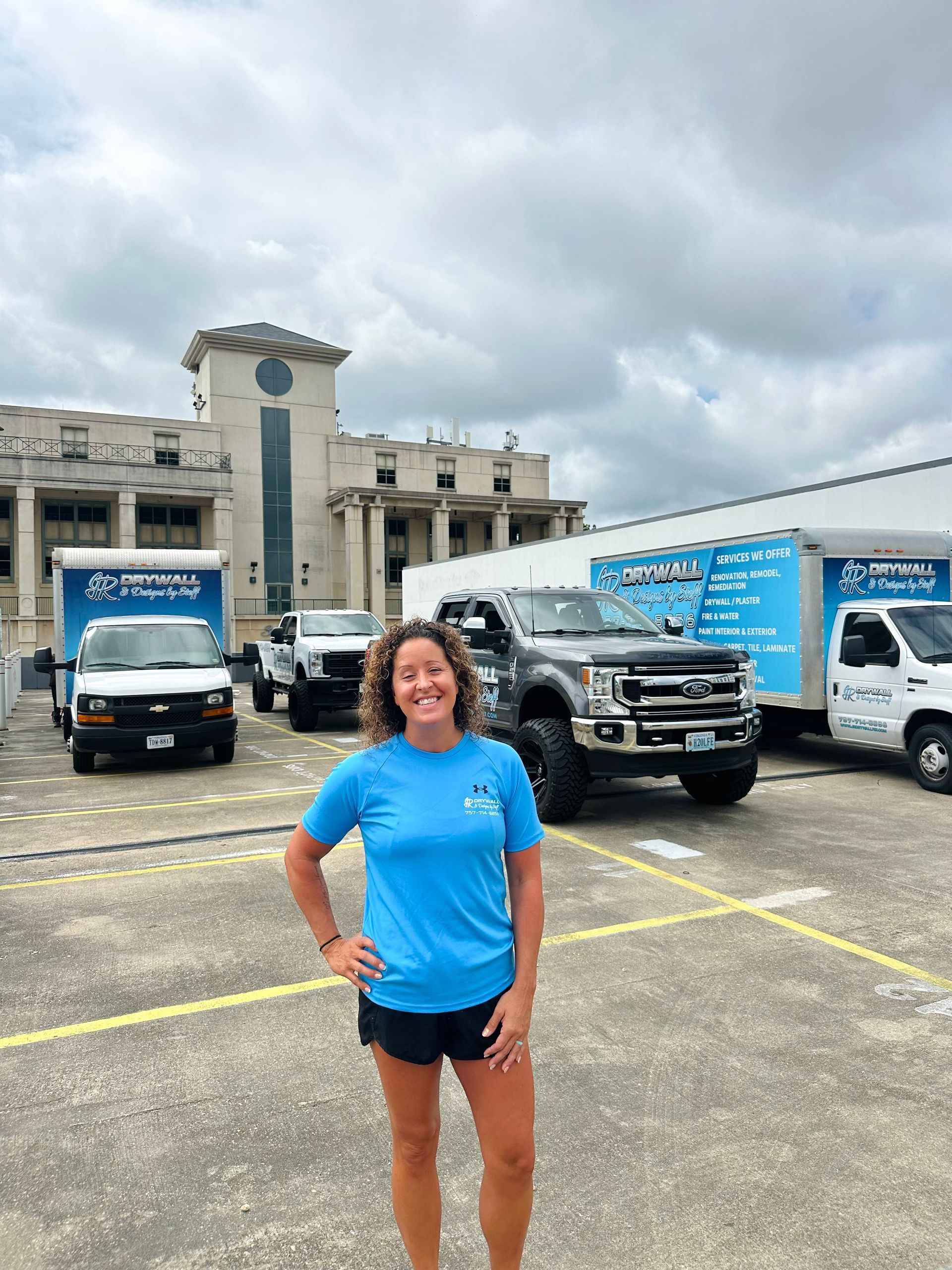 Woman in blue shirt poses in front of moving trucks and building.