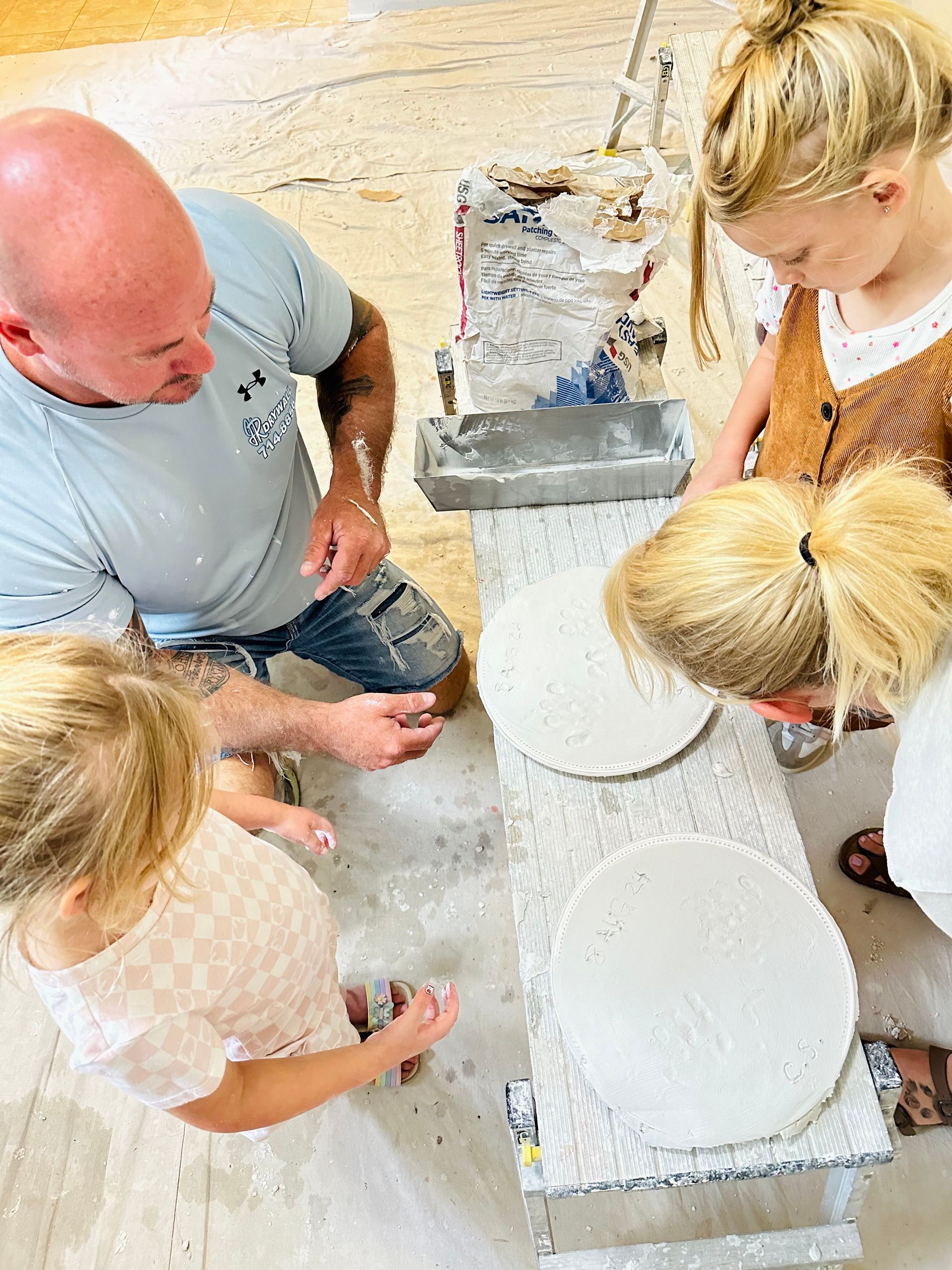 Man and two girls looking at circular, white art pieces; workshop setting.