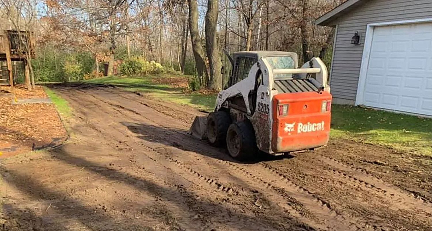a bobcat is driving down a dirt road next to a house .