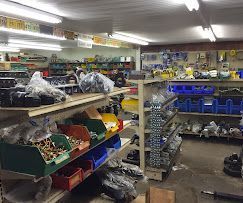 A hardware store interior with shelves stocked with automotive or mechanical parts in plastic bins and bags.