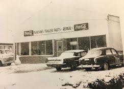 Black and white photo of Pearson's Trailer Parts & Repair store in snow, with two vintage cars parked in front.