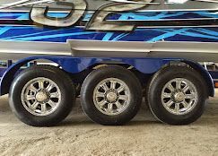A close-up view of the three chrome wheels and black tires of a blue and silver trailer parked on a concrete floor.