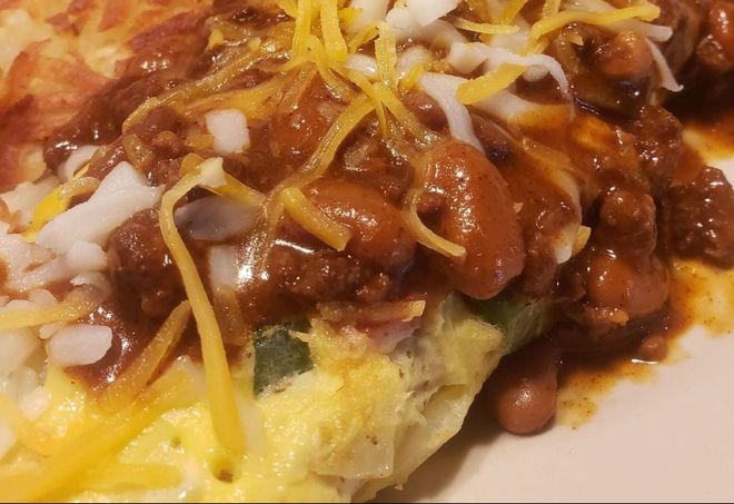 An omelet topped with chili, beans, shredded cheese, and diced white onions.