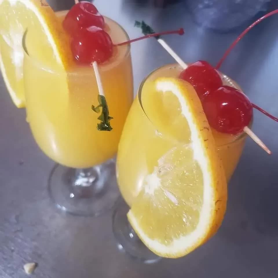 Two glasses of orange juice, each garnished with an orange slice and two maraschino cherries on a pick.
