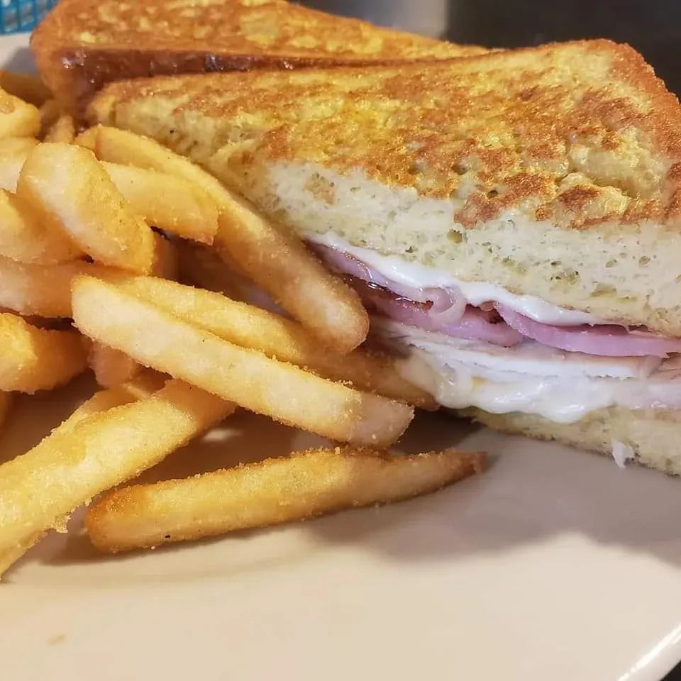 A Monte Cristo sandwich with ham and melted cheese on golden, egg-dipped bread, served with a side of crispy french fries.