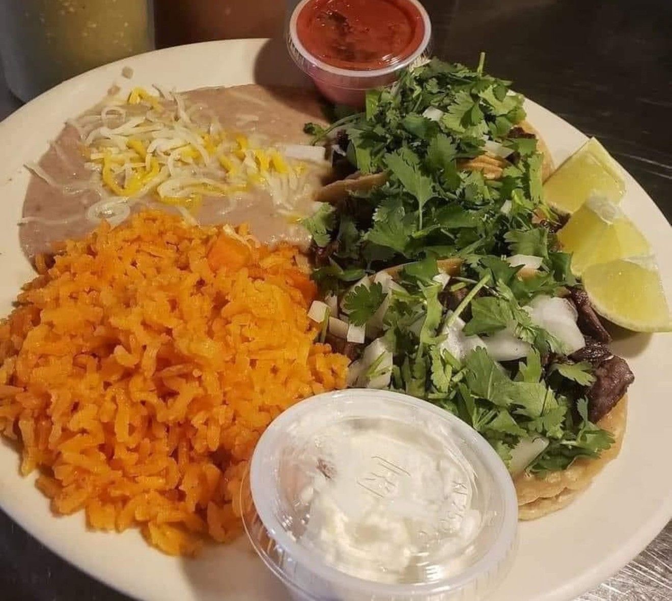 A plate of Mexican food featuring tacos topped with cilantro, side dishes of Spanish rice, refried beans, and salsa.