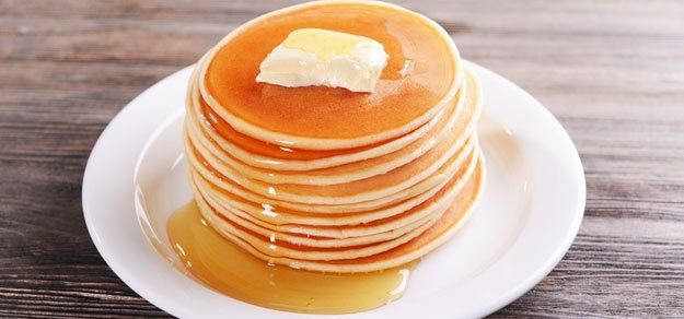 A stack of golden-brown pancakes topped with a pat of melting butter and maple syrup on a white plate.