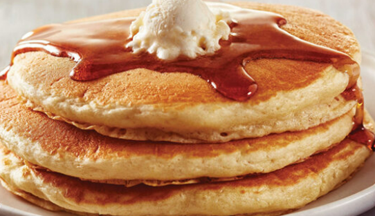 A stack of three golden-brown pancakes topped with a scoop of melting butter and drizzled with syrup on a white plate.
