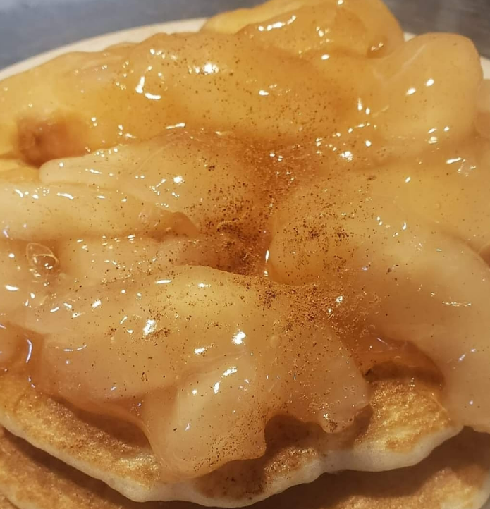 A stack of pancakes topped with a generous serving of cooked, cinnamon-dusted sliced apples.