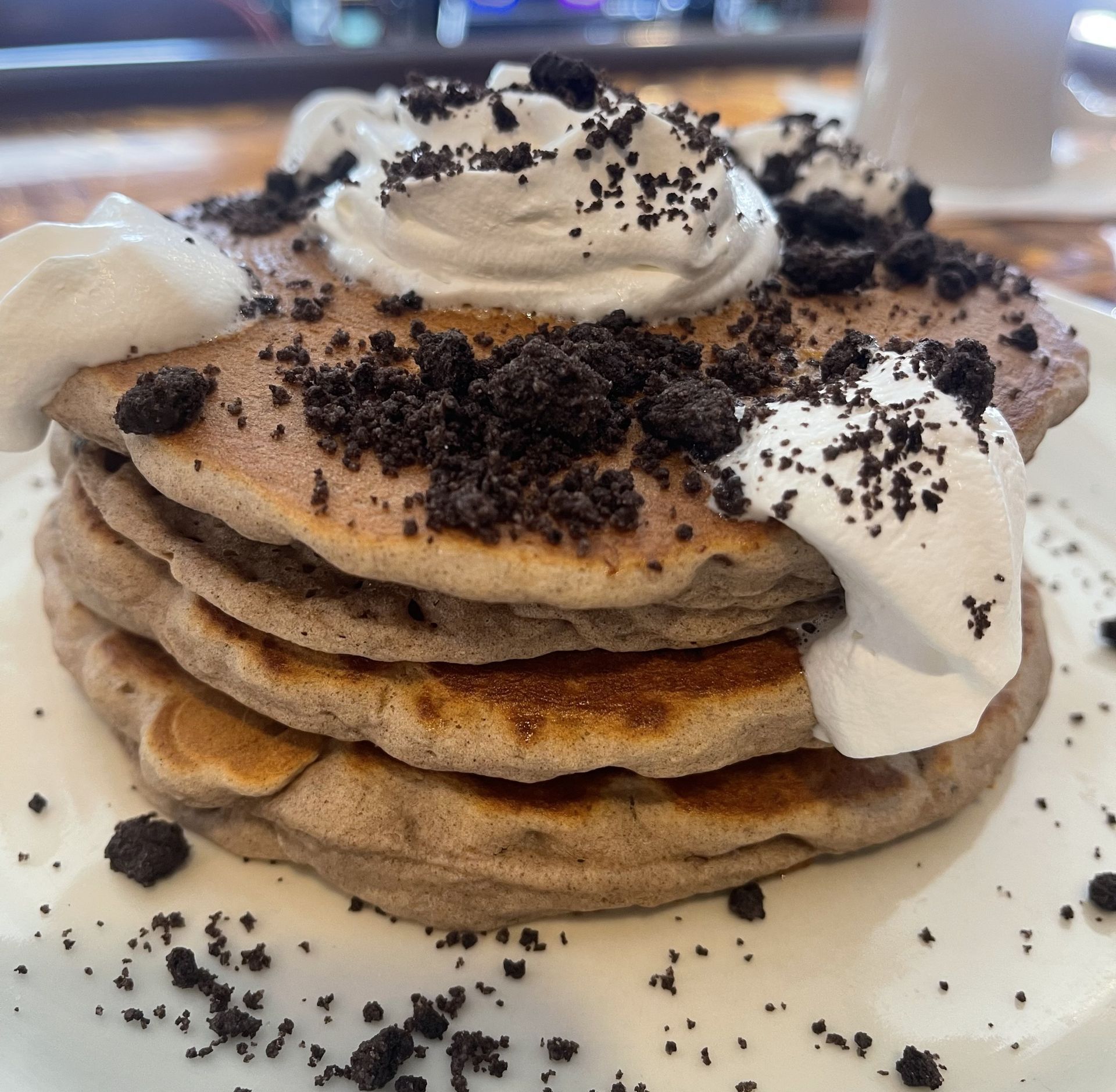 A stack of pancakes topped with whipped cream and crushed chocolate cookie crumbs on a white plate.