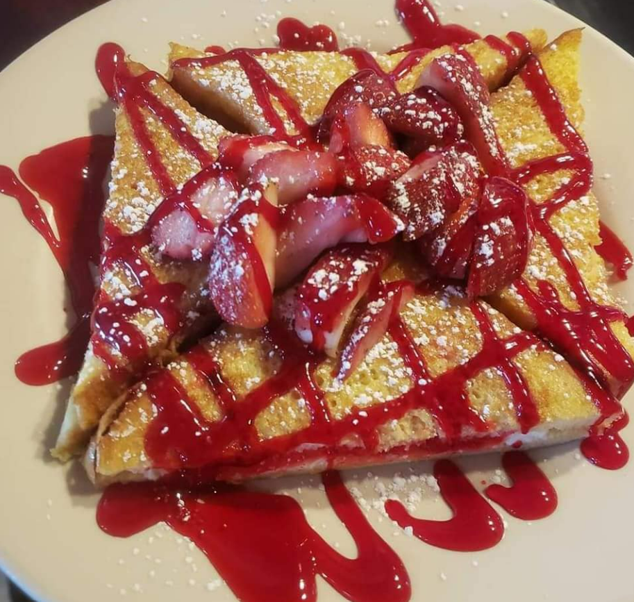 French toast slices topped with fresh strawberries, red syrup, and powdered sugar on a white plate.