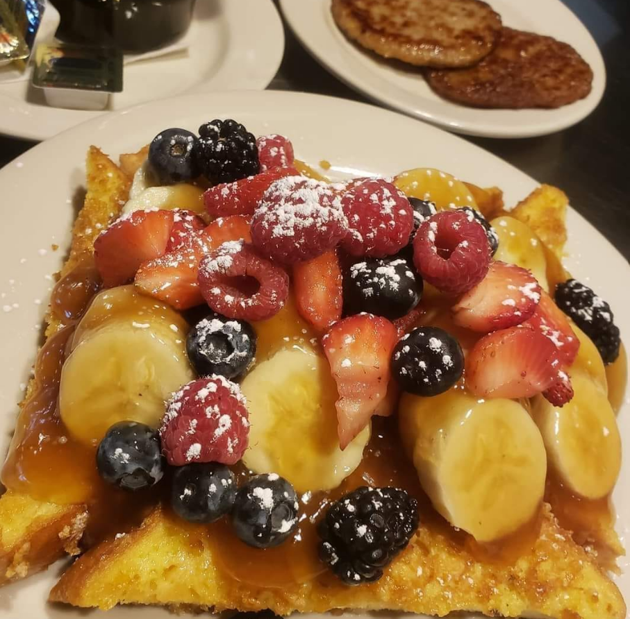 French toast topped with fresh strawberries, raspberries, blueberries, blackberries, sliced bananas, and powdered sugar.