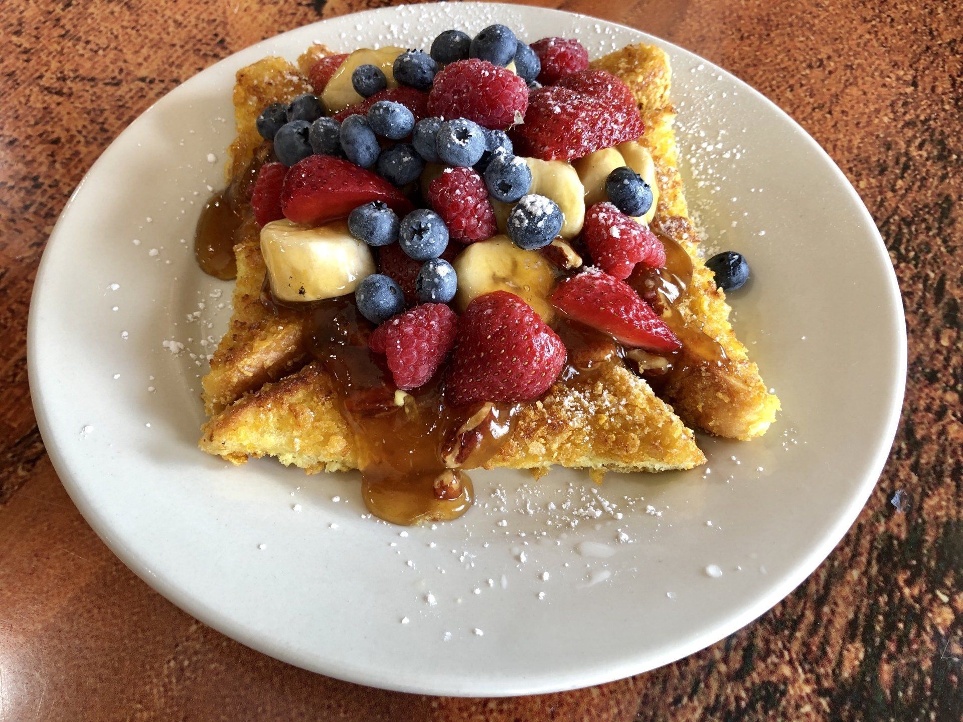 French toast topped with fresh strawberries, blueberries, and sliced bananas, drizzled with syrup and powdered sugar.