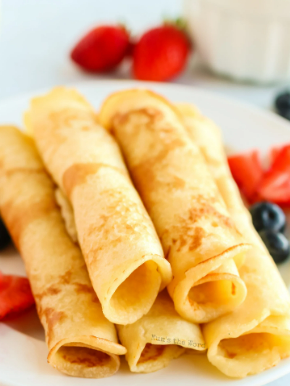 A plate of rolled crepes garnished with fresh strawberries and blueberries.